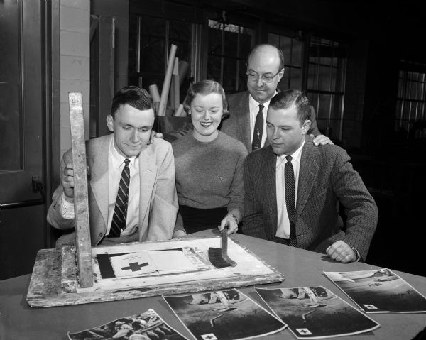 Three University of Wisconsin students work on a poster in preparation for a fundraising drive for the campus Red Cross. They are, from left: William Gage, Virginia Roby, and Richard Grossman. Looking on is Professor John. C. Hickman.