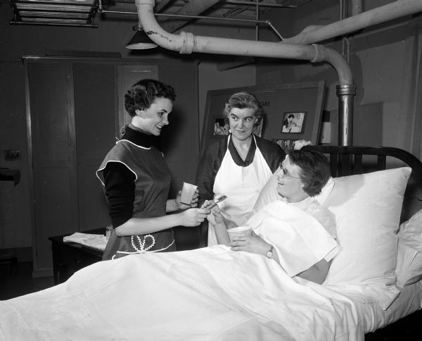 Ruth C. Adams, center, professor of Wisconsin School of Nursing and Red Cross instructor for the Home Care of the Sick program, is shown with two student nurses who portray a caregiver and patient. The students are Janet Stevens (left) of Duqoin, Illinois, and Carol Roberta, Milwaukee.