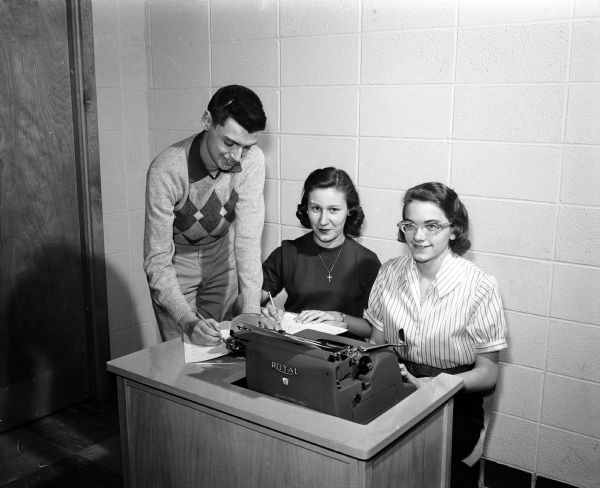 Three editors of the first year of the Monona Grove High School bi-monthly Eagle Post newspaper pose around a typewriter. They include Clare Sampley, Ruth Helmke, and Arlyss Perry.