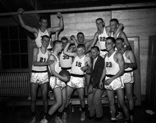The Wisconsin State High School basketball championship team from Shawano celebrates in the locker room. In the front row are: Loren Wolf, Larry Maltbey, John Cantwell, coach John Kenney, Guy Grignon, and Tom Koslowski. In the back row are: Dave Meyer, Bob Hammer, Fred Opperman, Marty Gharrity, and Mike Dodge.