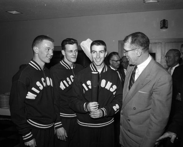 Bearers of the "Little Olympic" torch get instructions from Ivan Williamson (right), presenter of the service club awards. Left to right: Bjorn Thompson, Ed Jacobson, and Bob Brennan, members of the Wisconsin track team.