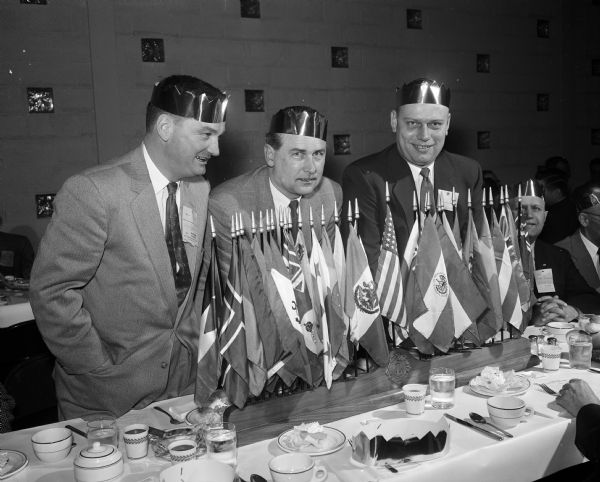 Three Madison service club champions stand behind flags commemorating nations during the Service Clubs' "Little Olympic" competition. Left to right: John Brickhouse, Roy Lampe, and Ed Berger.