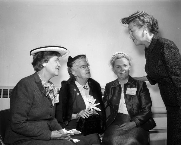 Four women attend the second annual convention of the Madison Diocesan Council of Catholic Women at Our Lady Queen of Peace Catholic Church. Seated, left to right, are: Mrs. Valentine Weber of Janesville, Mrs. Clara Flood of Darlington, and Mrs. Felix Bongiorno of Albany. Standing at right is Mrs. Joseph M. (Frances) O'Meara of Madison.