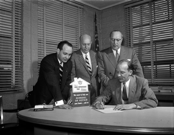 Madison mayor-elect Ivan Nestingen signs a proclamation announcing 1956 as "Home Improvement Year" as Marvin Reimann, Duane Bowman, and J. Jesse Hyman are looking on.