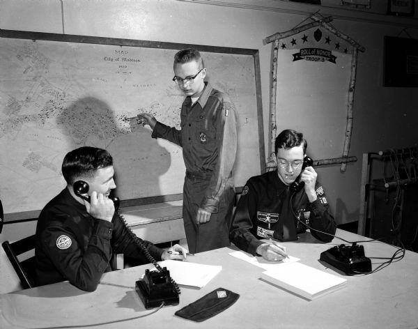 As part of a practice drill to prepare for possible disasters, phone calls are made to the crews of Explorer Post 503. Phoning are Gene Tschida (left), Explorer adviser and scout Tom Nichall. At center, scout Tom Trowbridge pin points the alleged disaster area on a map.