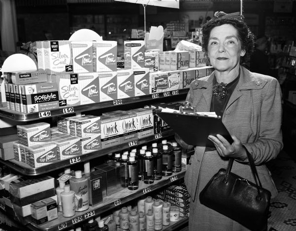 Nellie Howland, one of the five original members of the Philharmonic Chorus, is shown in a local drugstore as part of her job as inventory worker for the Market Research Company. The Philharmonic Chorus is celebrating its tenth anniversary.