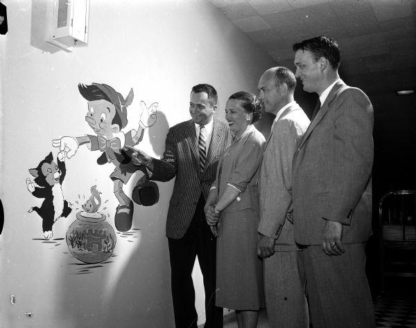 Dr. Richard B. Anderson points to one of the figures in the murals he did for the new pediatric unit at Madison General Hospital. Others in the photograph are (left to right): Mrs. K.W. (Myra) Kruger, president of the Madison General Women's auxiliary; Dr. William A. Tanner, chairman of the department of pediatrics; and Dr. Alex M. Iams, the previous department chairman.