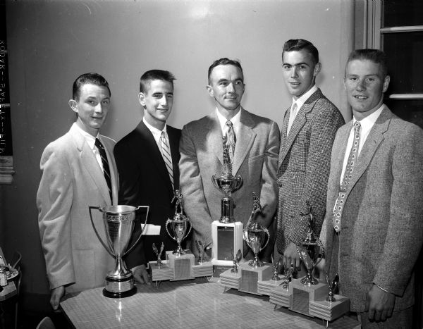 Five men pose behind five trophies. They include Coach Charlie Turner, Dave Hamel, Coach Hal Metzen, Gary Kielley, and Bill Thomas.