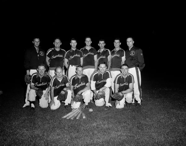 Group portrait of 12 men in softball uniforms with the team name "Frankie's" on their shirt fronts. Some are wearing baseball gloves and five bats are arrayed on the ground in front of them.