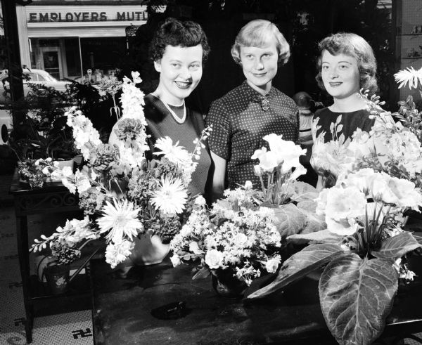 Selecting flowers for the Matrix banquet of the national Theta Sigma Phi convention are, from left: Mrs. Joseph (Felice) Goodman, 1015 Harrison Street, adviser in Beta chapter of Theta Sigma Phi at the University of Wisconsin and campus arrangements chairman for the convention; Miss Carol Schiller, Marshfield, co-decoration chairman for the banquet and Mrs Ronald Scott (OPolly Brobst), 211 Lathrop Street, co-editor of the Matrix Midget, a miniature publication for the dinner.