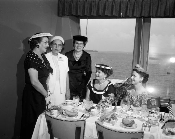 Visiting in front of a window overlooking Lake Mendota at the Edgewater Hotel during the regional brunch of the American Business Women's Association are Alma Frederick, Peoria, Illinois; Ann Bailey, Decator, Illinois; Florence Barrett, Kansas City, Kansas; Elsa Fagerstrom, Madison; and Edna Morris, Madison. Picnic Point is in the background.