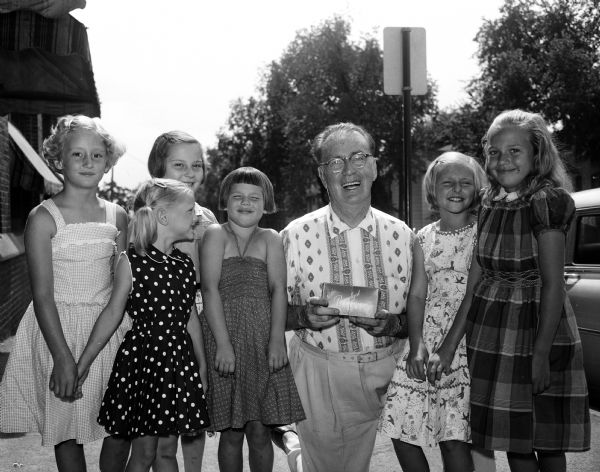 Joseph (Roundy) Coughlin, sports columnist for the <i>Wisconsin State Journal</i>, posing with six girls who raised money for the Roundy's Fun Fund by having a backyard carnival. Left to right: Marcia Steil, Siri Kitson, Jean Anderson, Pam McNitt, Roundy, Gina Kitson and Joan Jenson.