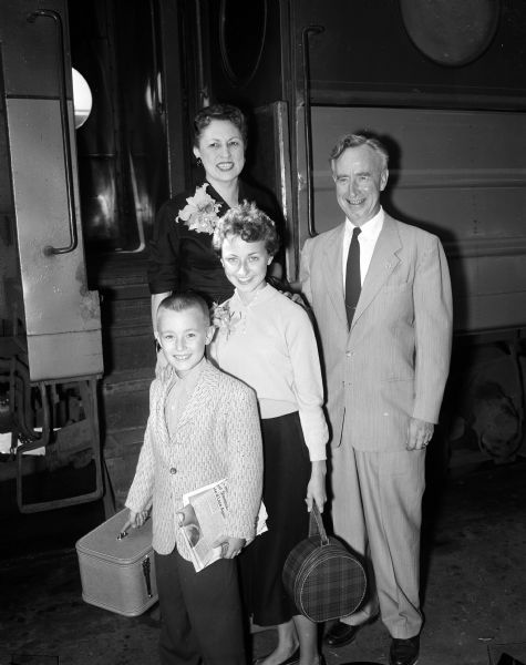 Helen and Vernon Thomson and two of their children, Tommy, age 9, and Susan, 14, posing in front of the steps of a passenger train car. They are traveling to the Republican convention in San Francisco, California. Attorney general of Wisconsin, Vernon Thomson, was also a Republican candidate for governor. The children are each holding small carry-on luggage cases and mother and daughter are wearing corsages.