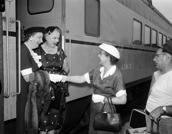 Glenn Wise (right) shaking hands and saying goodbye to two of her friends who are standing up on the step of a railroad passenger car. They are (left) Marian Fox and Inez Toebaas. Fox was national committeewomen-elect and vice-chairman of the Republican party of Wisconsin. Toebaas was an alternate delegate to the Republican convention in San Francisco, California. Mrs. Glenn (John E.) Wise, Wisconsin's secretary of state, was serving as acting governor while Governor Walter Kohler and Lt. Gov. Warren Knowles attended the convention.  Mrs. Fox has a mink stole draped on her arm and Mrs. Wise is wearing white gloves and a white hat.