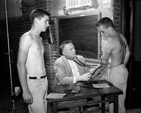 East High School football player Dick Borchardt, right, has his blood pressure taken by Dr. Theodore J. Nereim. Mike McCormick, left, another East High player, looks on.