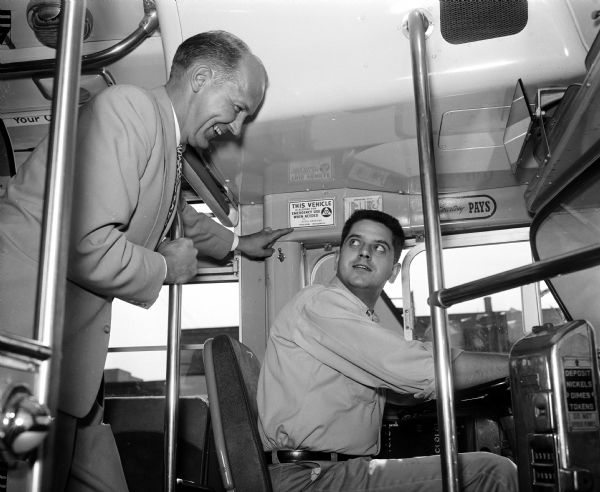 Mayor Ivan Nestingen points out one of the civil defense decals which are being placed on all Madison buses. The decals state that the buses are pledged for emergency when needed. The bus driver is Clifford Wood.