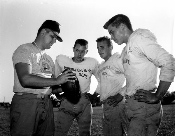Monona Grove High School football coach John Klement demonstrates a grip on the football to players Pete Mory, Dennis Howe, and Mike Cloutier during an early practice.