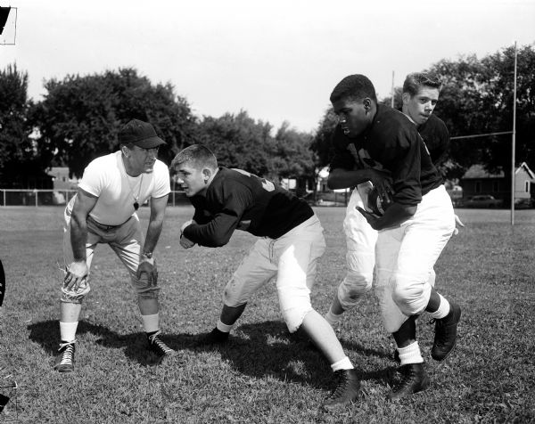 Madison Central High School football coach Harold (Gus) Pollock watches a backfield drill with center Chuck Muehlemann, quarterback Dick Pedracine, and halfback Al Smith during the first practice.