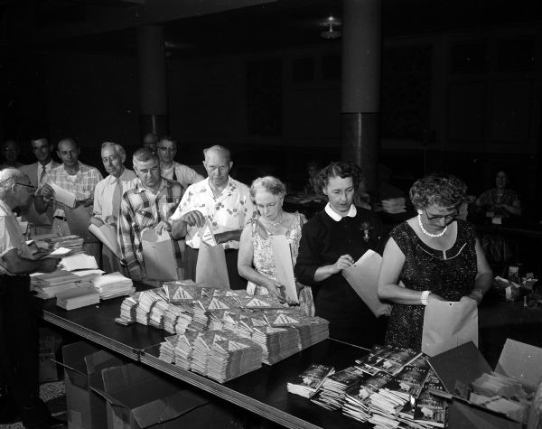 Shrine members and their wives at the Masonic Temple, assembling packets for the Midwest Shrine Convention. Left to right:  F.W. Born, C.H. Jorgensen, Arthur Strelow, Anthony Stock, William Reiter, Mrs. Fred Riddle, Vera Cnare, and Mrs. C.L. Barry.