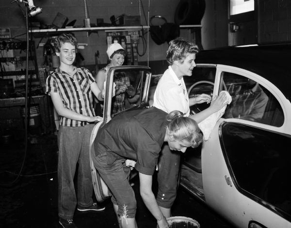 Four members of the Catholic Junior League polishing a car at George's Service Station, 5990 Monona Drive during an all-girl car wash at Madison service stations. Left to right: Donna Kurht, Eileen Uselmann, Mary Buenzli, and Joan Weber. The activity will finance league projects.