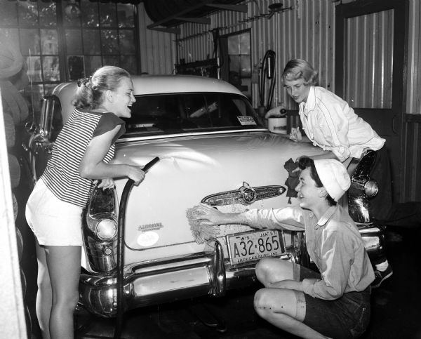 Three members of the Catholic Junior League wash a car at the Welsh and Aspinwall's D-X Station, 2035 University Avenue, during an all-girl car wash at Madison service stations. Left to right: Theresa Acker, Pat Putnam, and Kathleen O'Meara. The activity financed league projects.