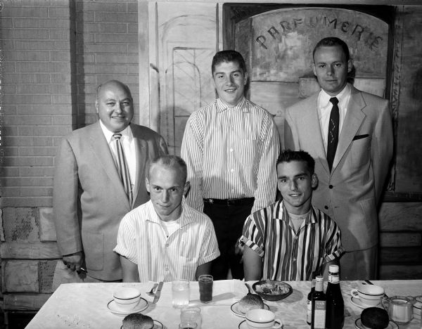 Group portrait of sponsor Ara Sergenian with managers and stars of his two championship teams in the Madison municipal baseball program. Left front: Frank Hebl, manager.  Right front:  Bill Hebl player. Back row left to right: Ara Sergeneian; Don Minor, manager; and Don Pond, player. Celebration dinner at Amato's.