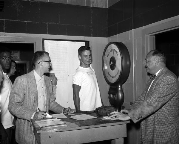 University of Wisconsin football player Gene Melvin weighs in at 163 pounds and is the lightest player on the 1956 team. At right is the <i>Wisconsin State Journal</i> sports editor Henry J. McCormick.