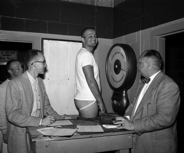 University of Wisconsin football player Bob Nelson weighs in at 239 pounds and is the heaviest player on the 1956 team. At right is the <i>Wisconsin State Journal</i> on sports editor Henry J. McCormick.