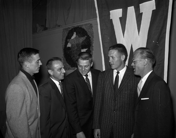Two Knights of Columbus council officials stand with three University of Wisconsin football players at the annual "Kickoff"  dinner of the Madison Council of the Knights of Columbus. Left to right: captain Pat Levenhagen; Wilfred Schlimgen, Grand Knight; fullback Frank Luksik; halfback Billy Lowe; and Art Flood, banquet program chairman.