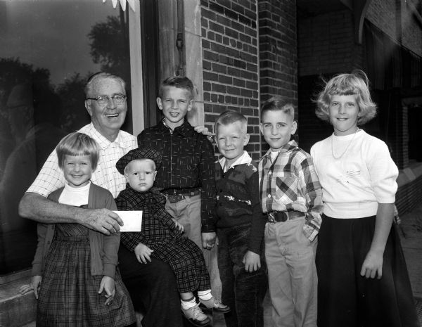 Six children from the Madison Westmorland neighborhood, who raised money for Roundy's charity for children, posing for a portrait with "Roundy" Coughlin. Left to right are: Madeline Goodrich, Chris Goodrich (on Roundy's lap), Jimmy Miller, Bill Goodrich, Bob Uhlmeyer, and Lynn Goodrich.