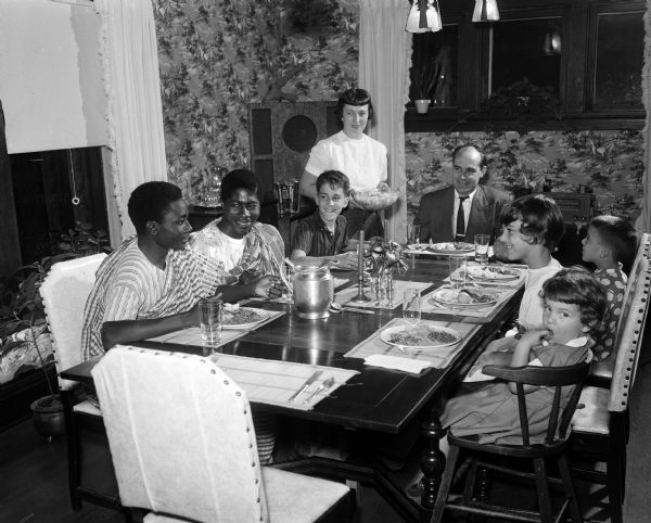 African students (left to right): Joseph Abrefa Ansah and Eugene Quaynor have dinner with Prof. Keith R. and Mary L. Symon and their four children, James, Judy, Keith, and Rowena, in the Symons' home. The Symons are members of the Madison Friends of International Students, whose mission is to give international students a view of informal American life.
