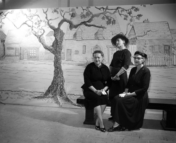Three members of the Women's Auxiliary pose beside a Wisconsin Historical Society exhibit of the Village Green. Left to right: Mrs. James H. Wegener, general chair of the Cornish Tea; Nada Besserdich, and Dorothy Schubert, President of the Women's Auxiliary of the Wisconsin Historical Society.