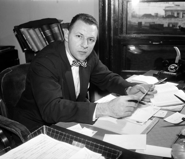 Portrait of Robert I. Perina, deputy district attorney of Dane county, seated at his desk. He assisted the Empty Stocking Club, an organized group dedicated to the cause of forgotten children, from two points of view: one way was through his duties in the district attorney's office and the other was through the charity work of his Marine Corps reserve unit.