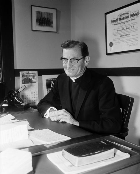 Portrait of Rev. E. J. Van Handel, Madison's Diocesan Director of the Catholic Welfare Bureau, sitting at his desk. Fr. Van Handel was also a promoter of the Empty Stocking club, which was a organized group dedicated to the cause of forgotten children.