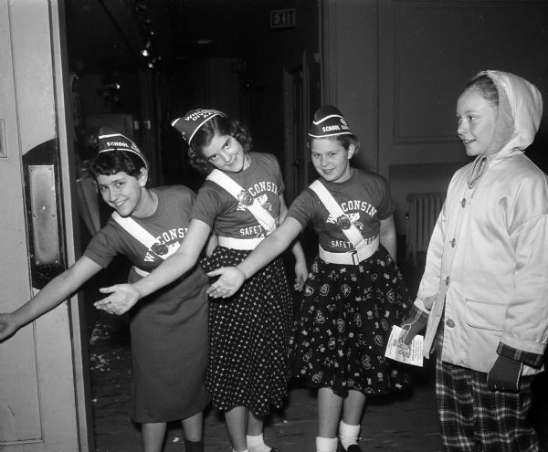 Three girls wearing Wisconsin Safety Patrol t-shirts and belts pretending to show a girl that it is all right to cross the street.