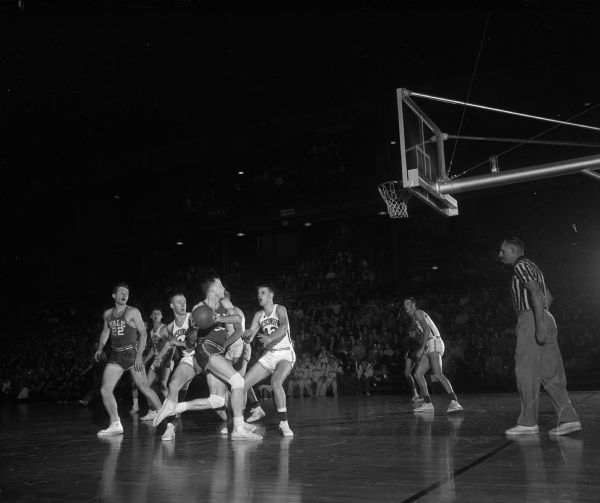 Action shot of Yale basketball players and a few of the University of Wisconsin basketball team on the court during a game.