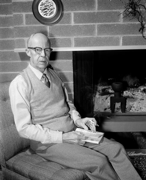 Don Halverson sitting by the fireplace in his home at 5022 Milward Drive that was designed to his specifications. He is the retired director of University of Wisconsin residence halls, and is a leading authority of residence hall operations and a professor and consultant in this field.
