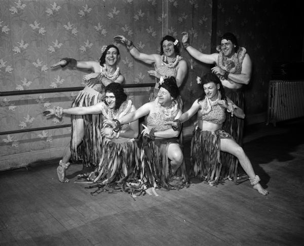 Six Jewish husbands dressed as female Hawaiian dancers in wigs and grass skirts posing for the camera. The husbands were part of a presentation at the annual Valentine benefit dinner dance of the Madison branch of the National Council of Jewish Women. They are, front row, left to right: Harry Tobias, Fred Lowe, and Joseph Silverberg. In the back row, shown left to right, are: William Stone, Orie Greenstein and Irvinr Yale Stein.