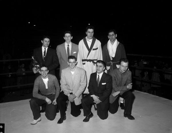 Group portrait of eight Tournament of Contenders boxing champions posed in the boxing ring following the event at the University of Wisconsin-Madison Field House. Front row, left to right: Allan Goodsitt, Milwaukee; John Drye, Monroe; Peter Spanakos, New York City; and Bob Judson, Chicago. Back Row: Bob Wilheim, Pampa, Texas; Charles Mohr, Long Island, New York; Bob Linke, Milwaukee, and Marshall Rand, Madison.