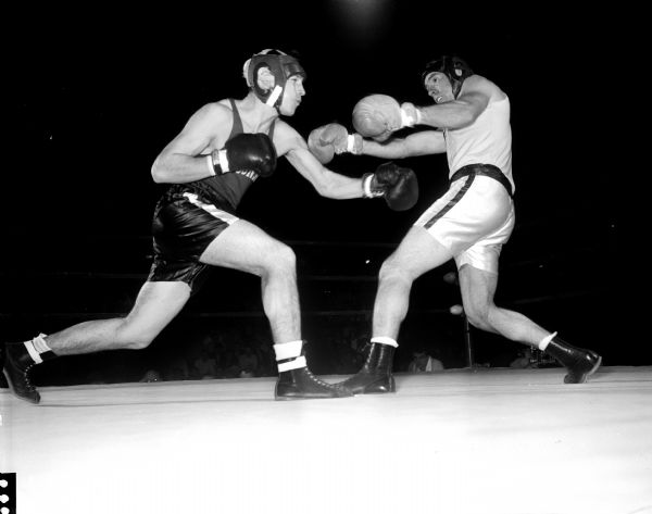 Action shot during the University of Wisconsin boxing tournament in the University of Wisconsin-Madison Field House. At left, Charlie Mohr, from Long Island New York, is throwing a left jab as Dave Cole, Prairie du Sac, backs away.  Mohr defeated Cole for the 165 pound crown.