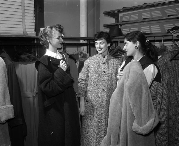 Three Med-Wives including Mrs. Finn (Patricia) Gunderson, 604 East Gorham Street; Mrs. Paul Stephl, 1930 East Main Street; and Mrs. Jordan (Phyllis) Fink, 135 East Johnson Street; are shown taking off their coats before volunteering at the Dane County Red Cross building. The Med-Wives is an organization composed of the wives of University of Wisconsin medical students.
