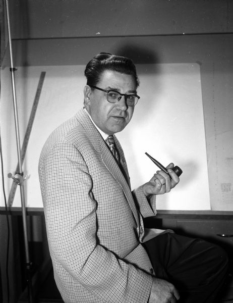 Portrait of George I. Wallace with pipe in hand. Wallace was a volunteer who served in many offices in area retardation (<i>sic</i>) councils. His two daughters, Virginia and Barbara, were born "normal", while his two sons, Bobby and Dickie, were born "Mongoloids" (<i>sic</i>). He also ran a sign business called 'Signs of Wallace' at 923 Regent Street.