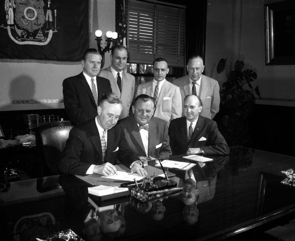 The photo caption states in full: "Gov. Vernon W. Thomson had an audience of six daylight saving time advocates when he signed into law the bill setting up a mandatory referendum on the issue for April 2nd. Left to right are: first row, Gov. Thomson, Lester Olseen, and Clarence Muth, and, in the second row: Lester Brann, and Assemblymen Earle Fricker (R-Milwaukee), Glen Pommerening (R-Wauwatosa), Harvey Abraham (R-Oshkosh)." The photo caption continues: "the three assemblymen are authors of the bill and the other three represent the Milwaukee Assn. of Commerce, which is opening a 'get-out-the-vote' drive in support of daylight saving time. If Wisconsin voters approve on April 2nd, the state will go on daylight saving time each summer, beginning April 29."