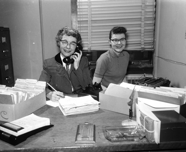 Madison families offer rooms to teenagers attending the annual State Basketball Tournament. Full-time help takes reservations and information. Mildred Coleman, left, is shown at the telephone taking housing reservations and Donallee Haworth, right, staff secretary of the Community Welfare Council and the Madison Youth Council, types the information.