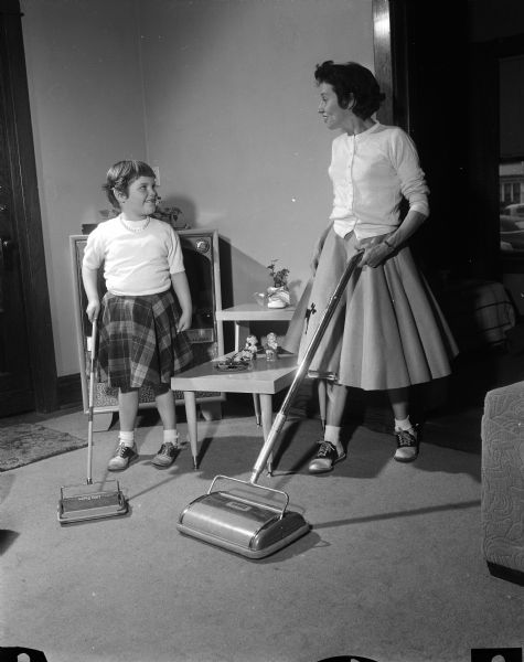 Winnie Delamater and her daughter Sandra, age 6, use carpet sweepers to clean in their home. Winnie and her husband Roland were both seriously physically handicapped by cerebral palsy since birth and met at Camp Wawbeek. The camp provides a camping experience for physically handicapped adults and children. It is maintained by the Wisconsin Association for the Disabled and funded by the sale of Easter Seals.