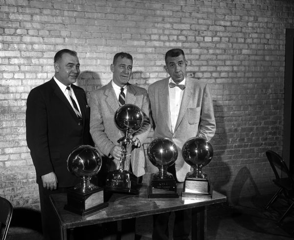 The University of Wisconsin's Athletic Department hosts the coaches and players in the annual WIAA state basketball tournament. Shown with the state meet trophies are, left to right:  George Lanphear, public relations director; Ivan Williamson, Athletic director; and Harold E. (Bud) Foster, Badger basketball coach.