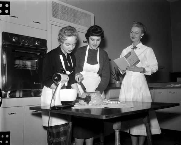 Mary Crain (right), home economist, teacher, dietician, and manager of the West High School cafeteria, supervises two of her students, Linda Gaarder and Alice Bolgrien, as they frost an angel food cake.