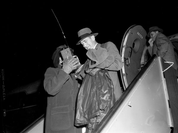 Football coach Ivy Williamson (?) is interviewed by a man with a radio transmitter on the steps of the airplane upon his return from the Rose Bowl game.