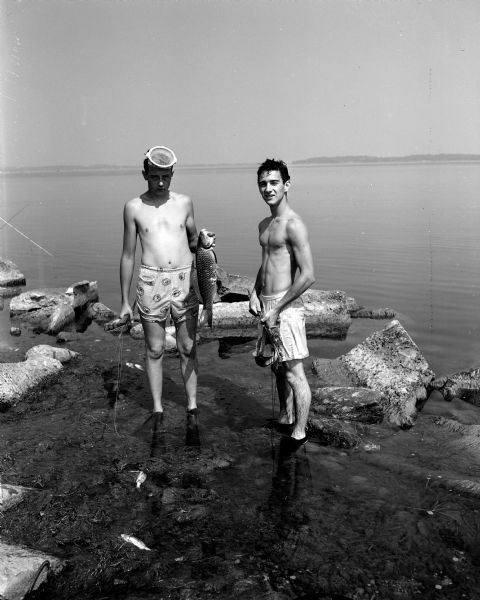 Dick Charmley and Gary Davies standing on the shore of Lake Mendota with a fish (carp) they caught while spear fishing.