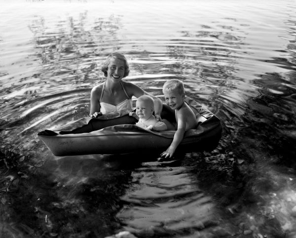 Bette Sonneland and her children, Kim (age 3) and Kristin (9 months), enjoying Lake Mendota in a rubber boat near the home of Bette's parents, Dr. and Mrs. Edwin F. Scneiders of 19 Fuller Drive.